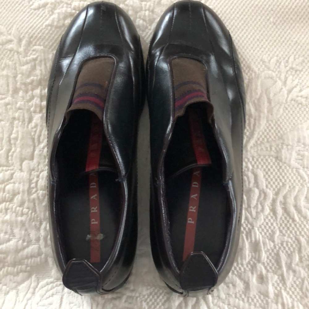 PRADA black loafers with red  accents on the flap.